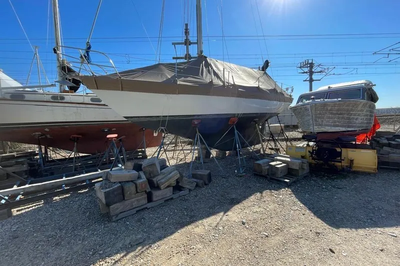 Slide: The Image of 1981 Cape Dory 33 sailboat on stands, covered, in a boatyard under clear blue sky. - 3