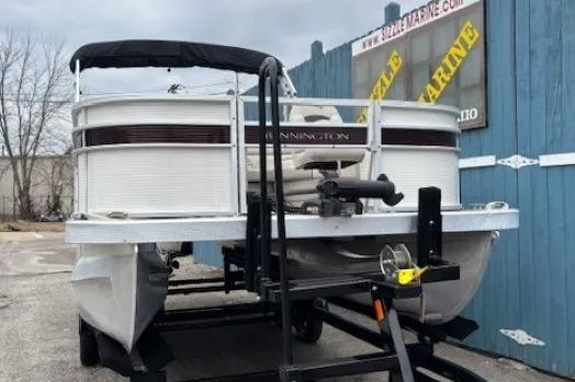 Slide: The Image of 2019 Bennington S 20 SFNP pontoon boat on trailer, parked near blue building. - 2