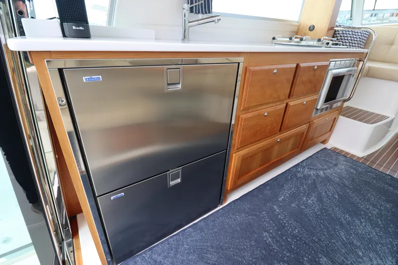 Slide: The Image of 2019 Back Cove 41 yacht kitchen with stainless steel fridge, wooden cabinets, and microwave. - 14
