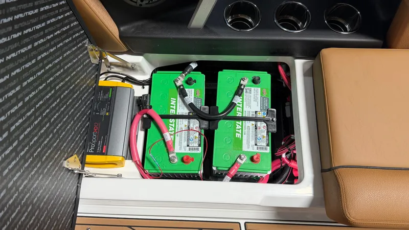 Slide: The Image of Battery compartment with two green batteries and wiring, surrounded by brown upholstery and cup holders. - 37