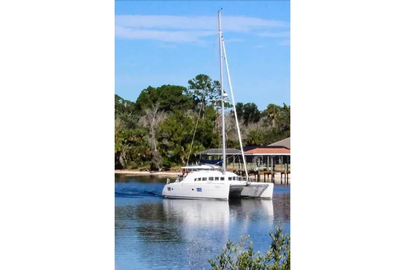 Slide: The Image of 2006 Lagoon 410-S2 catamaran sailing on a calm river near a wooded shoreline. - 43