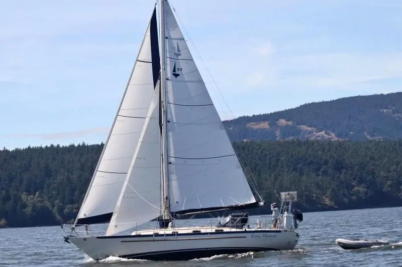The Image of 1990 Pacific Seacraft PSC 37 sailboat cruising on a scenic lake with forested hills. - 1