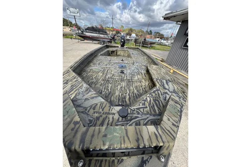 Slide: The Image of 2026 SeaArk 1752 Slayer X Pro boat with camouflage design, parked outdoors under cloudy skies. - 5