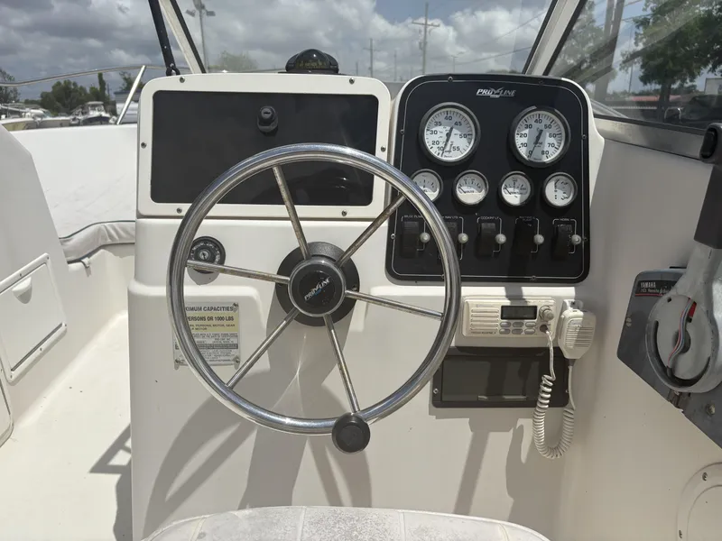 Slide: The Image of 1996 Pro-Line 202 boat dashboard with steering wheel and gauges under a cloudy sky. - 6