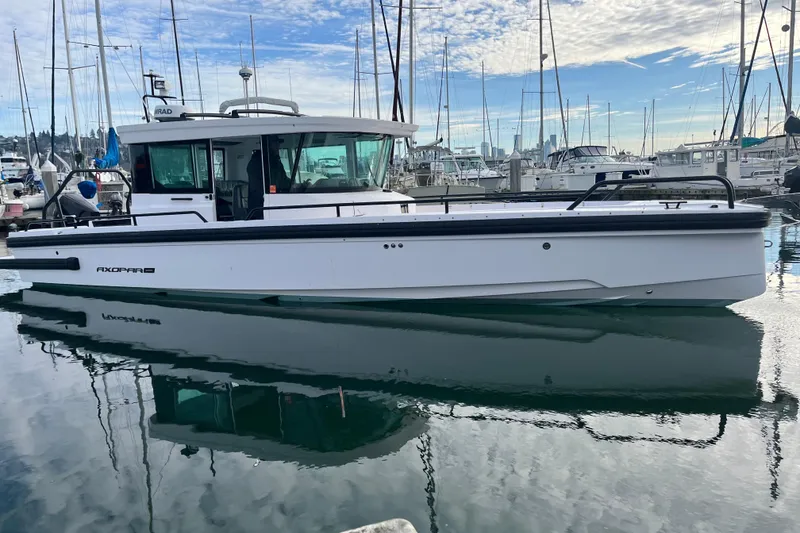 Slide: The Image of 2021 Axopar 28 Cabin boat docked in a marina, reflecting on calm water. - 1