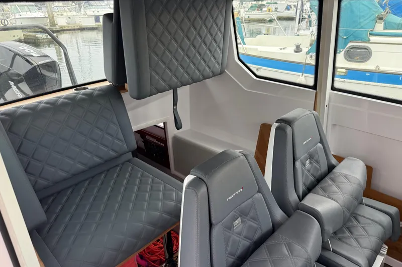 Slide: The Image of 2021 Axopar 28 Cabin interior with quilted gray seating and windows overlooking marina. - 27