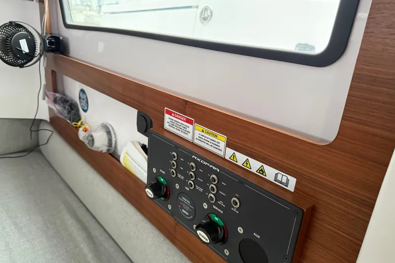Slide: The Image of 2021 Axopar 28 Cabin interior control panel with wood finish and safety labels. - 30