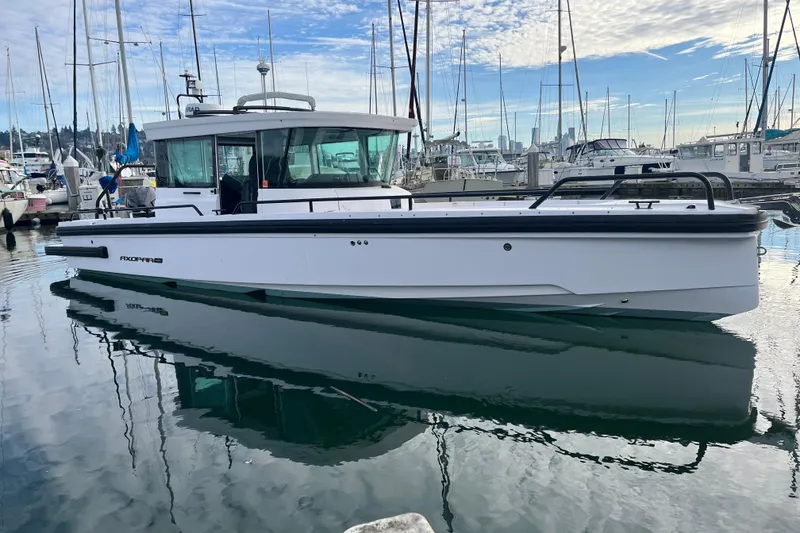 Slide: The Image of 2021 Axopar 28 Cabin boat docked in a marina, reflecting on calm water. - 46