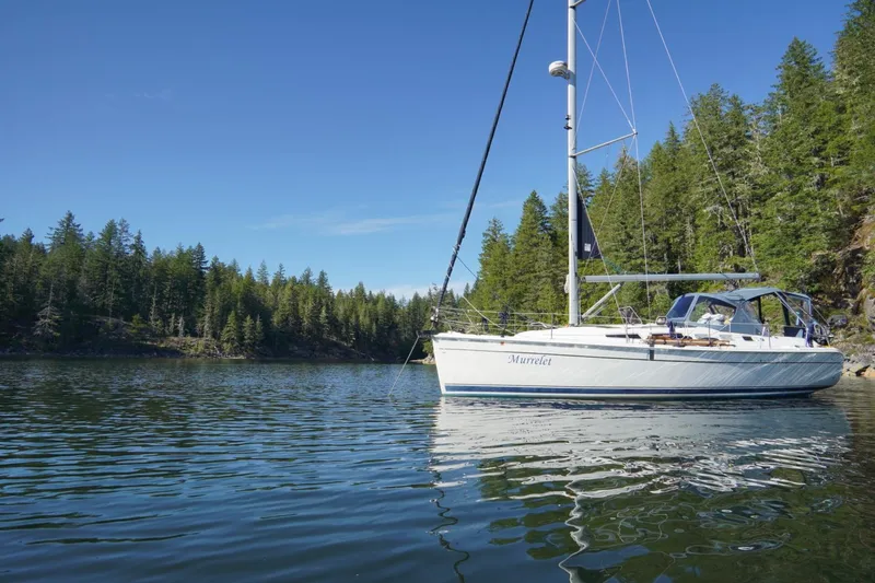 Slide: The Image of Sailboat "Murrelet" on calm water, surrounded by lush forest, under clear blue sky. Hunter 38, 2009. - 23