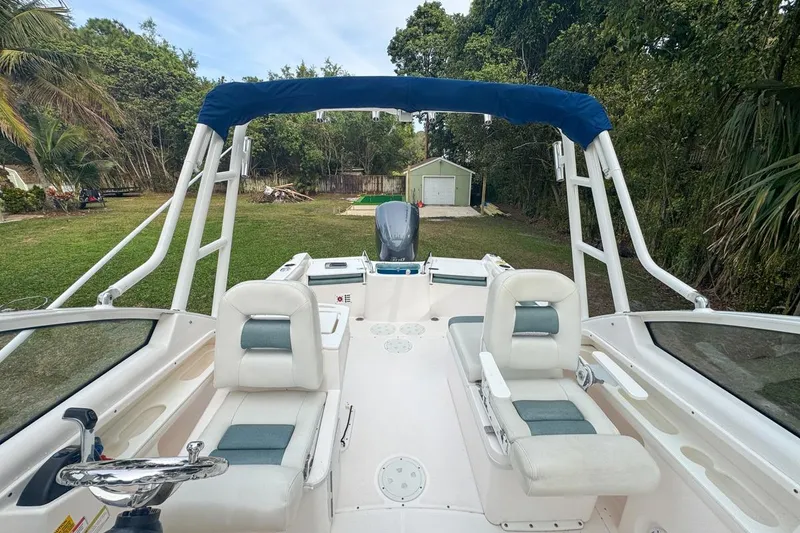 Slide: The Image of 2014 Everglades 230 Dual Console boat with seating, steering wheel, and canopy in a grassy yard. - 63
