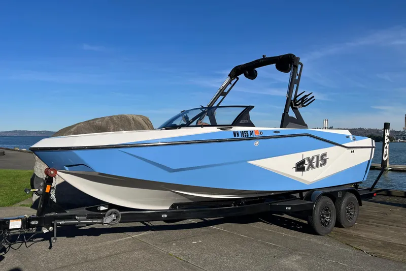The Image of 2024 Axis T220 boat on trailer by the water, blue and white design. - 1