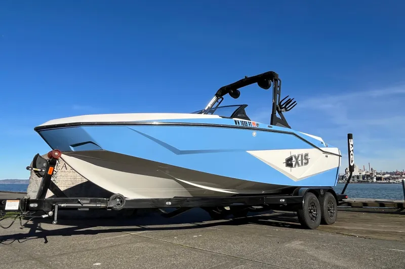 Slide: The Image of 2024 Axis T220 boat on trailer by waterfront, clear blue sky background. - 2