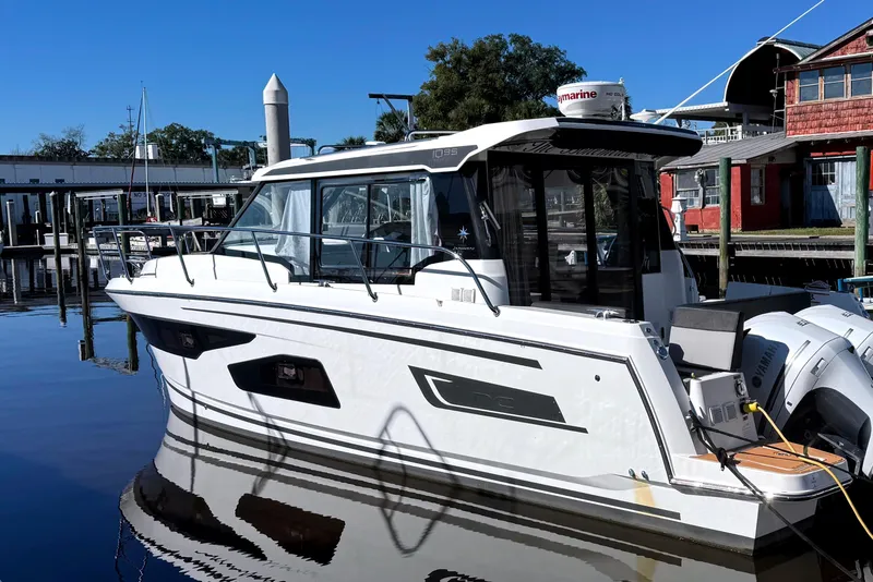 The Image of 2021 Jeanneau NC Weekender 1095 docked at a marina, reflecting on calm water. - 0