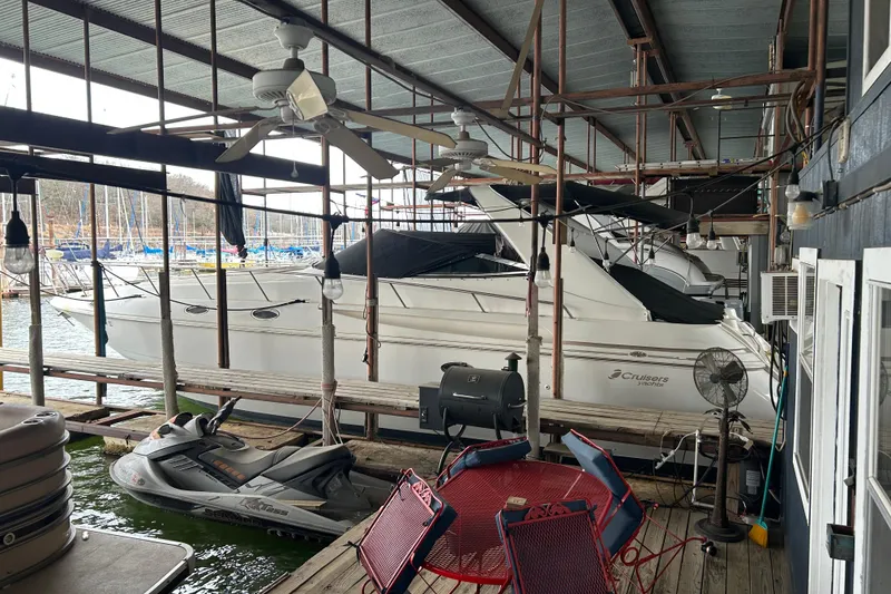 The Image of 1998 Cruisers Yachts 4270 Express docked in a covered marina with a jet ski nearby. - 0