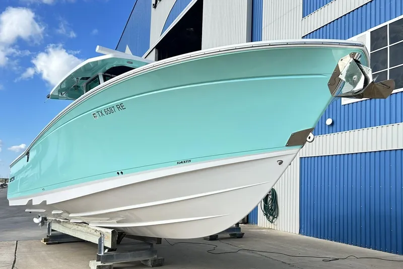 The Image of 2023 Blackfin 332 CC boat in light blue, docked near a blue building. - 0