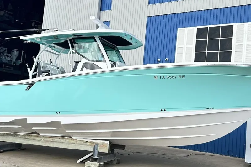 Slide: The Image of 2023 Blackfin 332 CC boat in light blue, docked near a blue and white building. - 5