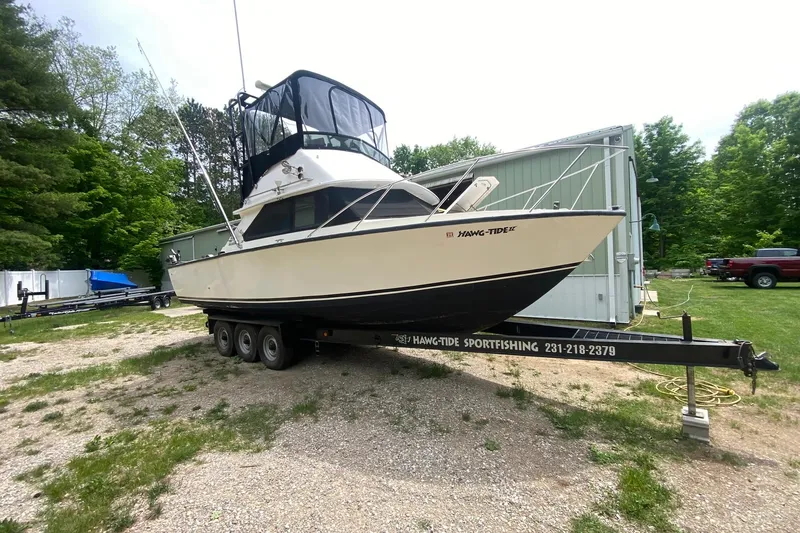 Slide: The Image of 1977 Bertram 28 Flybridge boat on trailer, surrounded by greenery and parked near a building. - 3