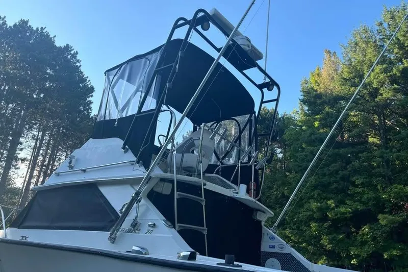 Slide: The Image of 1977 Bertram 28 Flybridge boat with canopy, surrounded by trees under clear blue sky. - 7