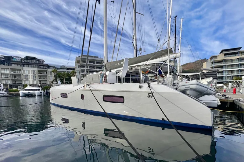 Slide: The Image of 2017 Outremer 51 catamaran docked in marina with modern buildings in background. - 2