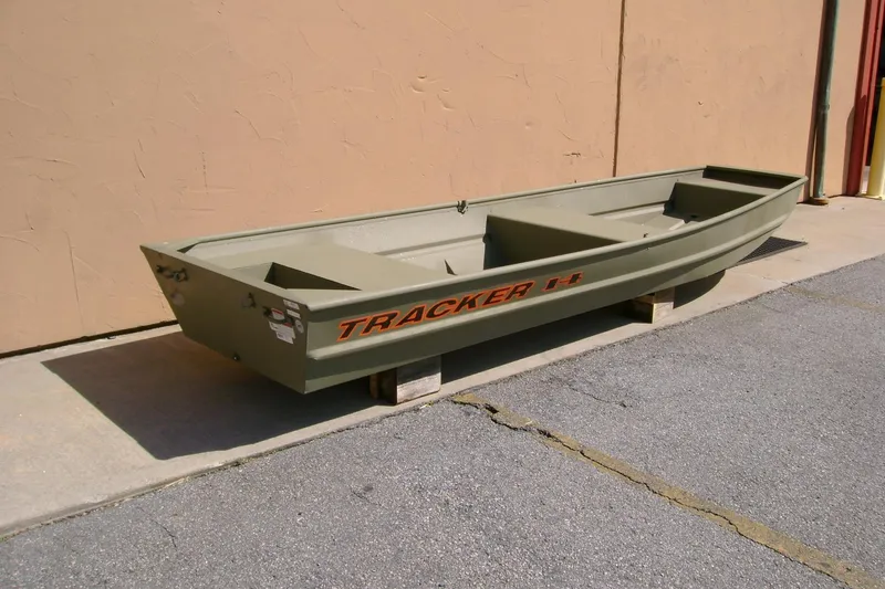 Slide: The Image of 2026 Tracker Grizzly 14 Jon boat in olive green, displayed outdoors on wooden blocks. - 2