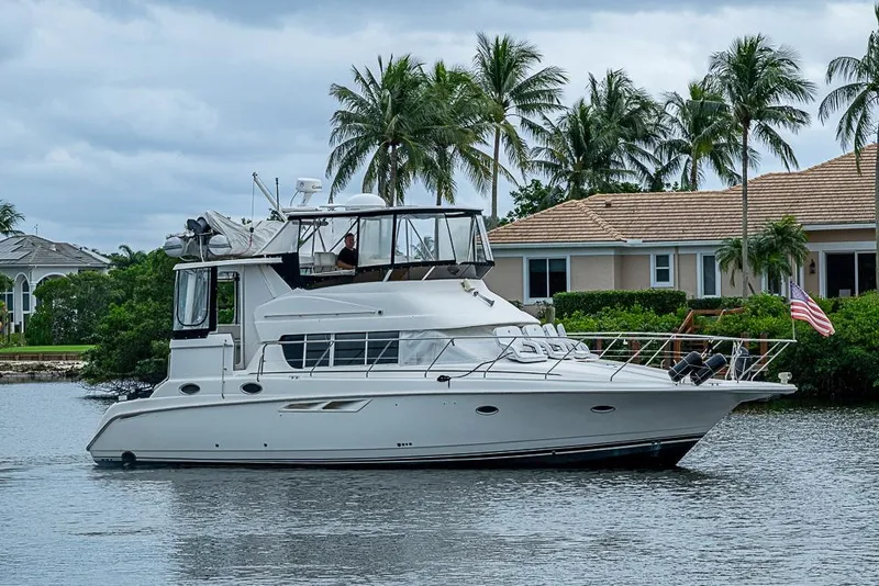 Slide: The Image of 2000 Silverton 442 Cockpit Motor Yacht cruising near waterfront homes and palm trees. - 2