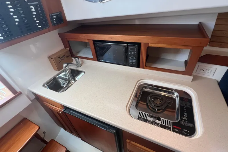 Slide: The Image of 2005 Back Cove 29 boat galley with sink, stove, microwave, and wooden cabinetry. - 51
