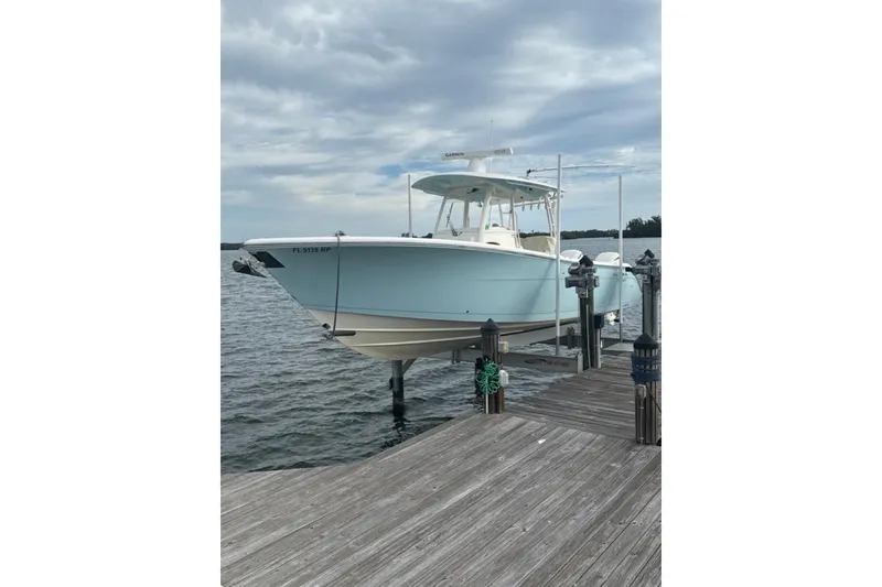 Slide: The Image of 2018 Cobia 320 Center Console boat docked on a lift by the water. - 10