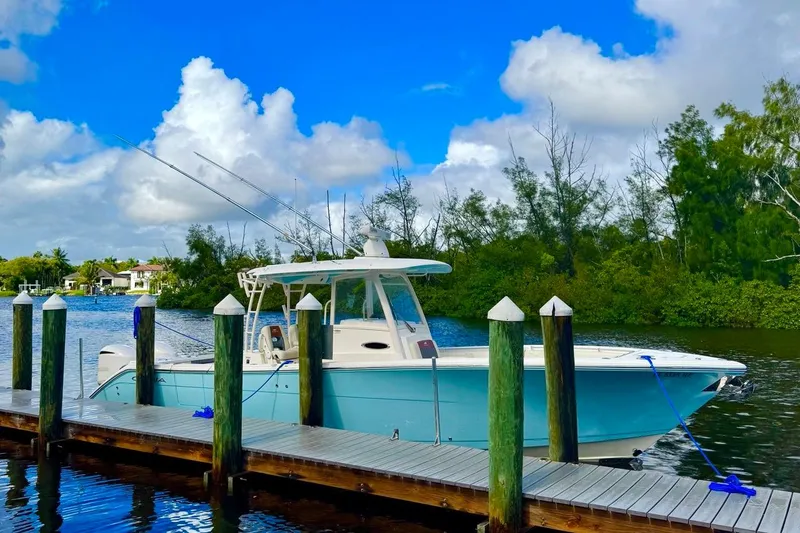 Slide: The Image of 2018 Cobia 320 Center Console boat docked by a scenic waterfront. - 8