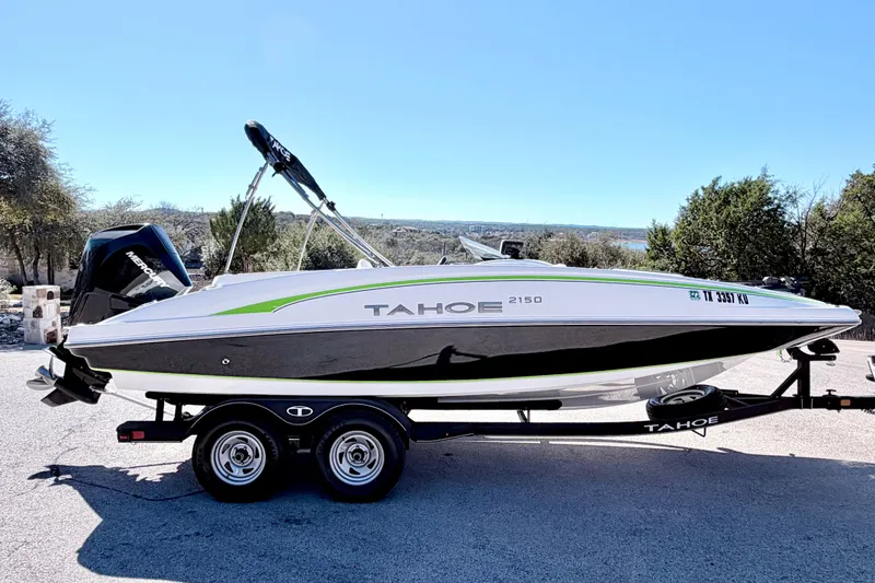 Slide: The Image of 2023 Tahoe 2150 boat on trailer, parked outdoors with trees in background. - 14