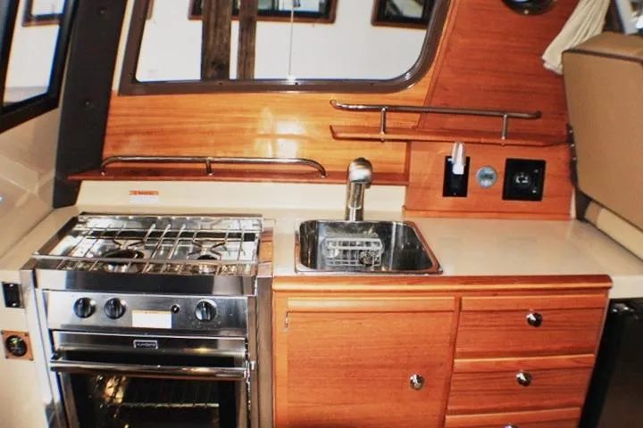 Slide: The Image of 2020 Ranger Tugs R-27 boat kitchen with stove, sink, and wooden cabinetry. - 64
