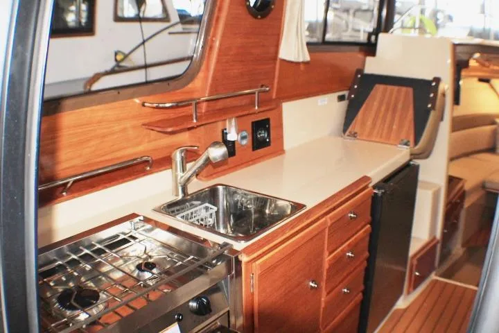 Slide: The Image of 2020 Ranger Tugs R-27 interior kitchen with wood cabinetry and stainless steel appliances. - 66
