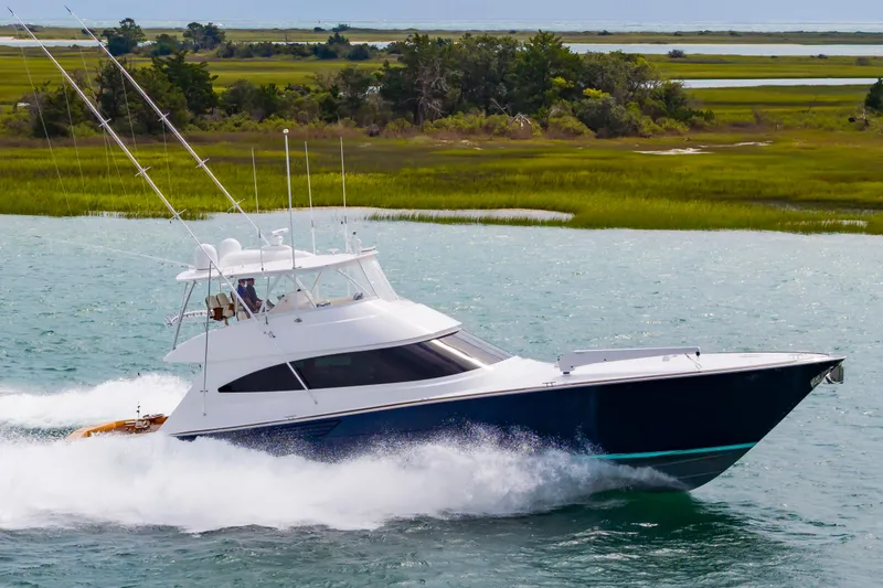 Slide: The Image of 2024 Viking 72 Convertible yacht cruising on water near lush green landscape. - 16