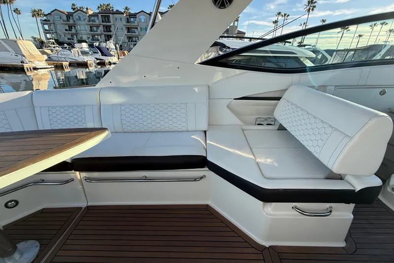 Slide: The Image of 2019 Sea Ray 320 Sundancer interior with white seating and wooden deck in marina setting. - 9