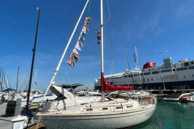 Slide: The Image of 1986 Pearson 303 sailboat docked at marina, adorned with colorful flags under clear blue sky. - 1