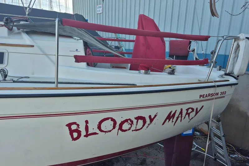 Slide: The Image of 1986 Pearson 303 sailboat named "Bloody Mary" docked near a storage building. - 17
