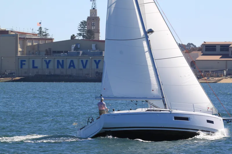 Slide: The Image of 2026 Beneteau Oceanis 37.1 sailing near a "FLY NAVY" building on a sunny day. - 14