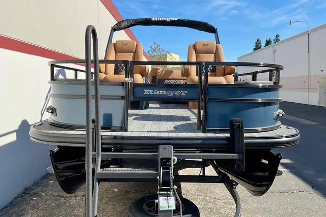 Slide: The Image of 2026 Ranger Reata 220F pontoon boat with tan seats, parked outdoors. - 1
