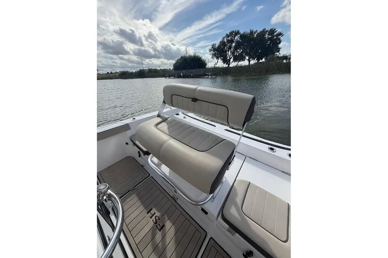 Slide: The Image of 2022 Yamaha Boats 210 FSH Sport interior with seating, on a calm lake under a cloudy sky. - 11