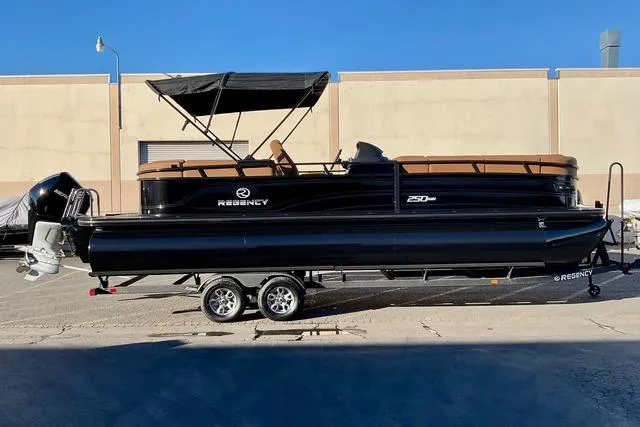 The Image of 2026 Regency 250DL pontoon boat on trailer, black with tan seating, parked outdoors. - 0