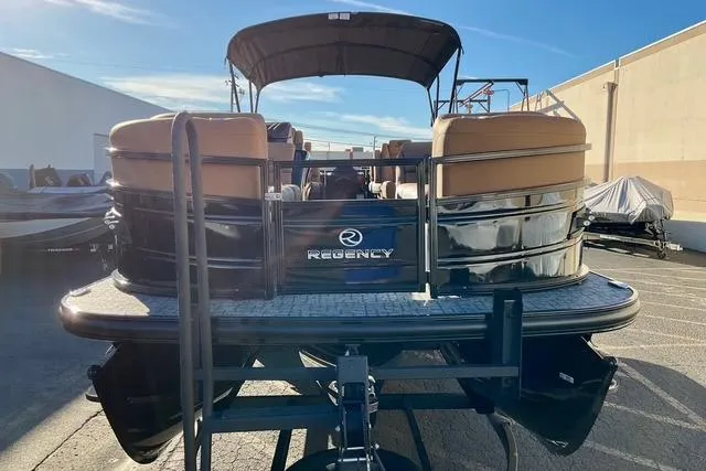 Slide: The Image of 2026 Regency 250DL pontoon boat, rear view, parked outdoors under clear sky. - 2
