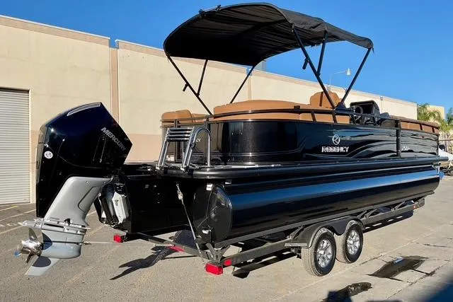 Slide: The Image of 2026 Regency 250DL pontoon boat with Mercury outboard engine, parked on a trailer. - 7