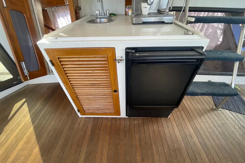 Slide: The Image of 1990 Spindrift Cockpit Motoryacht interior with kitchenette, featuring sink, wooden cabinet, and mini fridge. - 29