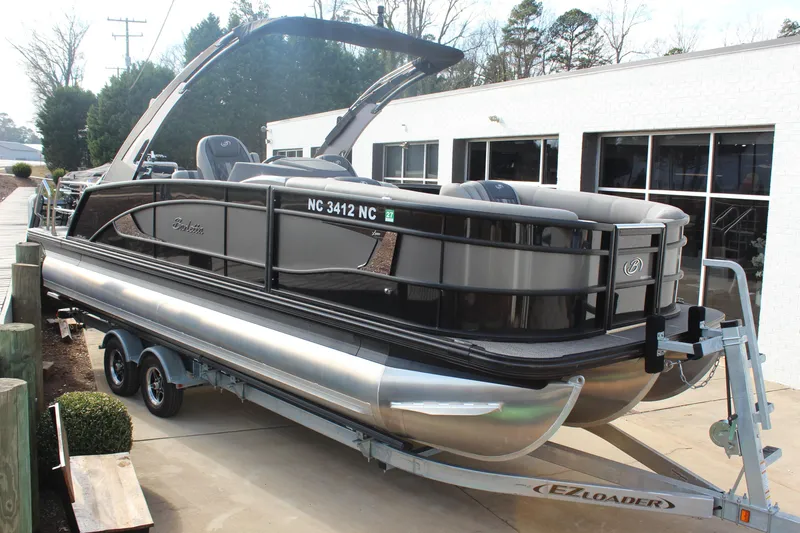 The Image of 2024 Barletta Lusso 23UC pontoon boat on trailer, parked outside a building. - 1