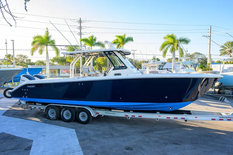 Slide: The Image of 2023 Pursuit S 328 Sport boat on trailer, parked outdoors with palm trees. - 3