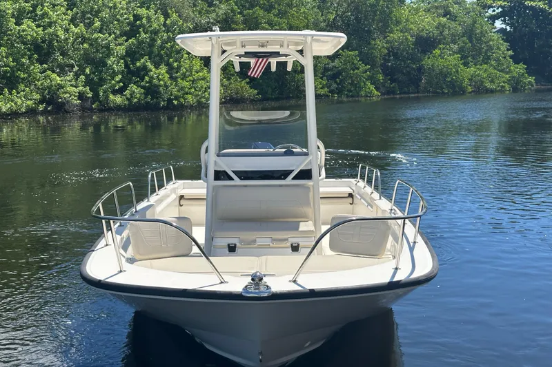 Slide: The Image of 2022 Boston Whaler 210 Montauk boat on calm water, surrounded by lush greenery. - 2