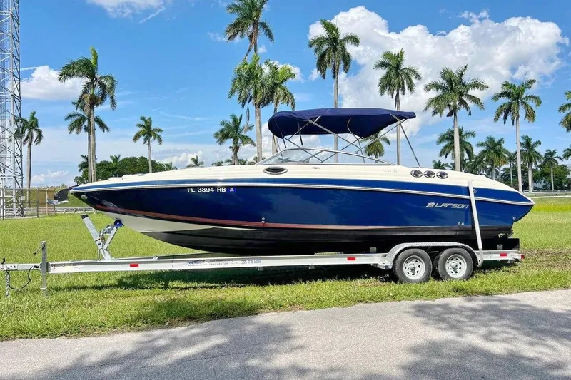 Slide: The Image of 2013 Larson LXi 292 IO boat on trailer, parked near palm trees under blue sky. - 2