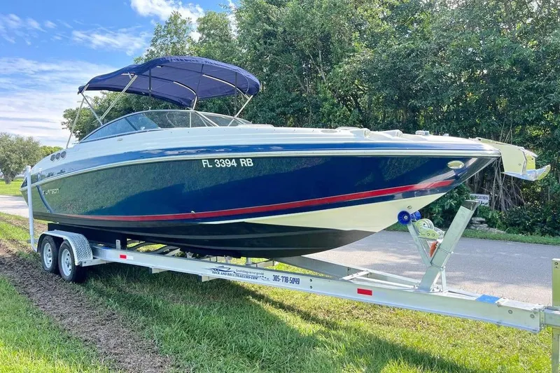 Slide: The Image of 2013 Larson LXi 292 IO boat on trailer, parked near trees and road. - 6