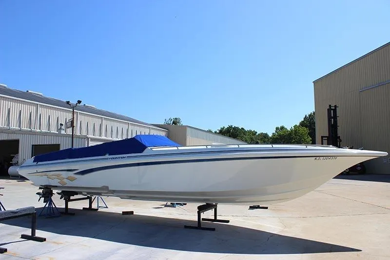 The Image of 2000 Fountain 32 Fever speedboat with blue cover on a stand outdoors. - 0