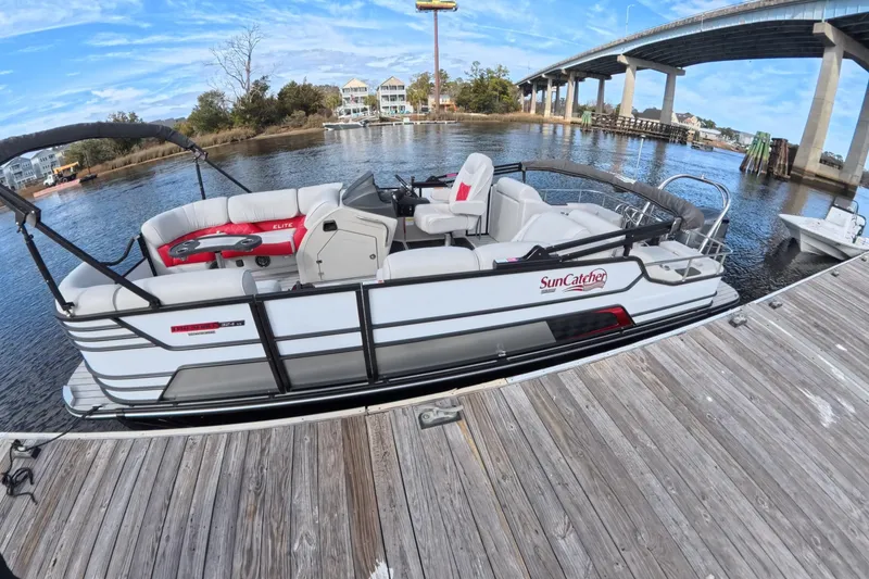 Slide: The Image of 2025 SunCatcher ELITE SERIES 324 SS pontoon boat docked by a scenic bridge. - 10