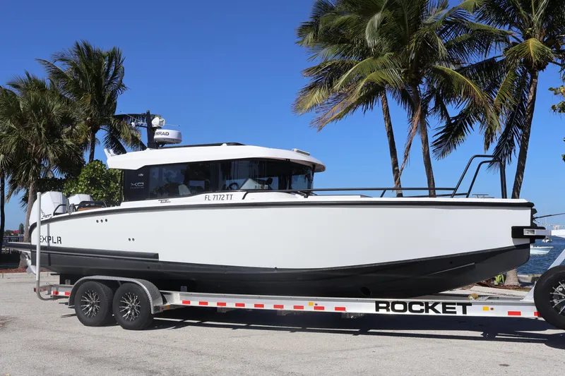 Slide: The Image of 2024 XO Boats EXPLR 10 S Plus on trailer, palm trees in background. - 2